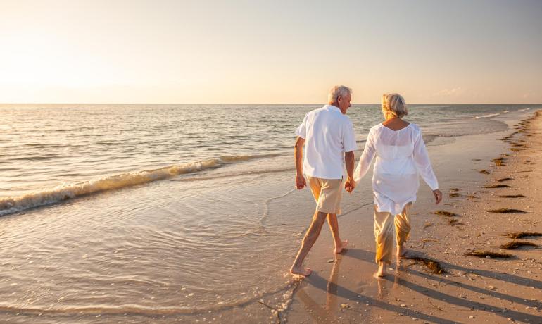 Älteres Paar geht bei Sonnenuntergang am Strand spazieren, Hand in Hand.