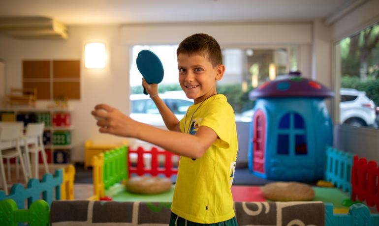 Bambino gioca a ping pong in una sala giochi colorata.